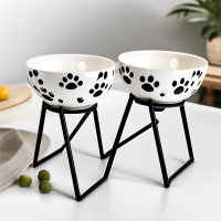 AA set of ceramic food bowls on stands, 2 bowls included: 1 with a paw pattern, 2 with a fish pattern. There is an individual black stand for each of the bowls. Use offers: profitable, easy to wash, safe materials, durable materials